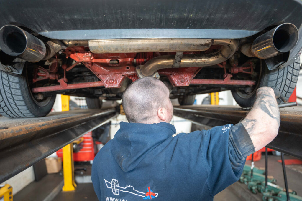 mechanic underneath a car with tailpipes