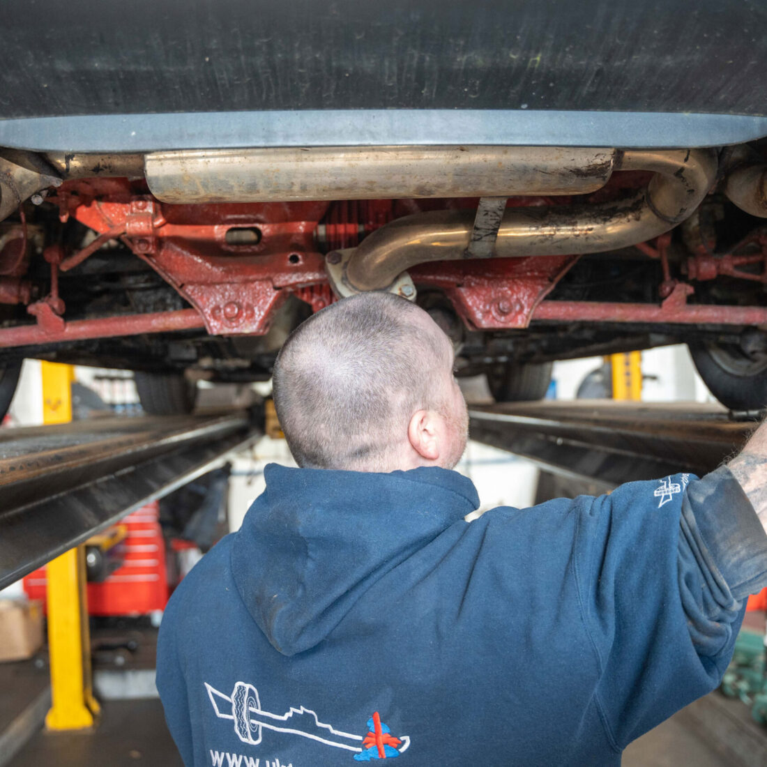 mechanic underneath a car with tailpipes